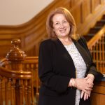 A photo of Sharon Butler smiling in front of a staircase