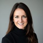 Photo of Ann Marie Scheidegger wearing a black shirt and smiling against a gray background.