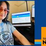 Irene Oramas Sosa wears a blue tee shirt and rose-tinted glasses in a selfie with her work computer screen. Her hair is dark and long, and she is smiling.