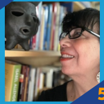 Smiling woman in glasses looking at a black mask sculpture on a bookshelf, next to SUNY Empire 5 Minute Feature logo.