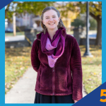 Person smiling outdoors in a maroon jacket and purple scarf.