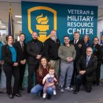 A photo of a group of people in front of a wall that says "Veteran and Military Resource Center"