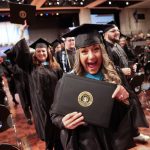 A photo of a graduate holding up a diploma cover at a graduation ceremony