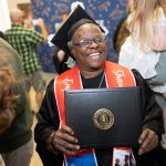 A photo of a graduate holding up a diploma cover and smiling.