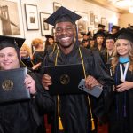 Students holding diploma covers, wearing regalia and smiling.