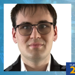 Centered head-and-shoulders portrait of Joseph Caroselli wearing glasses, a white shirt, and a dark jacket on a light background. Blue graduation-themed frame with a torch logo at top left and ‘Class of 2026’ banner at bottom right.