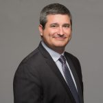 Photo of a man in suit against a gray background.